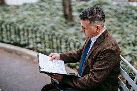 Man in formal attire reviewing documents on a park bench on a cool day.