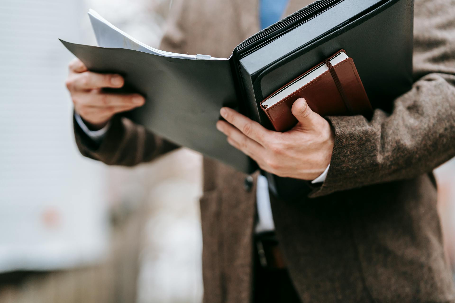 A professional in formal attire holding a notepad and folder outside, emphasizing business and focus.