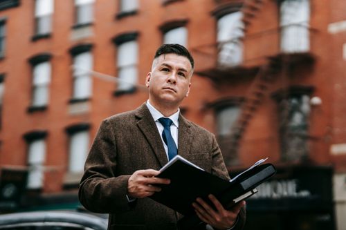 Free Businessman in a formal suit holding documents outside an urban building. Stock Photo