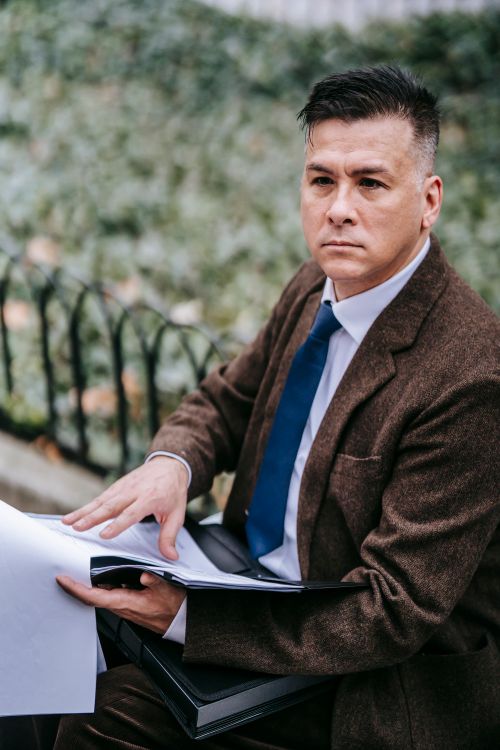 Free A pensive businessman in formal attire reviewing documents in an outdoor setting. Stock Photo