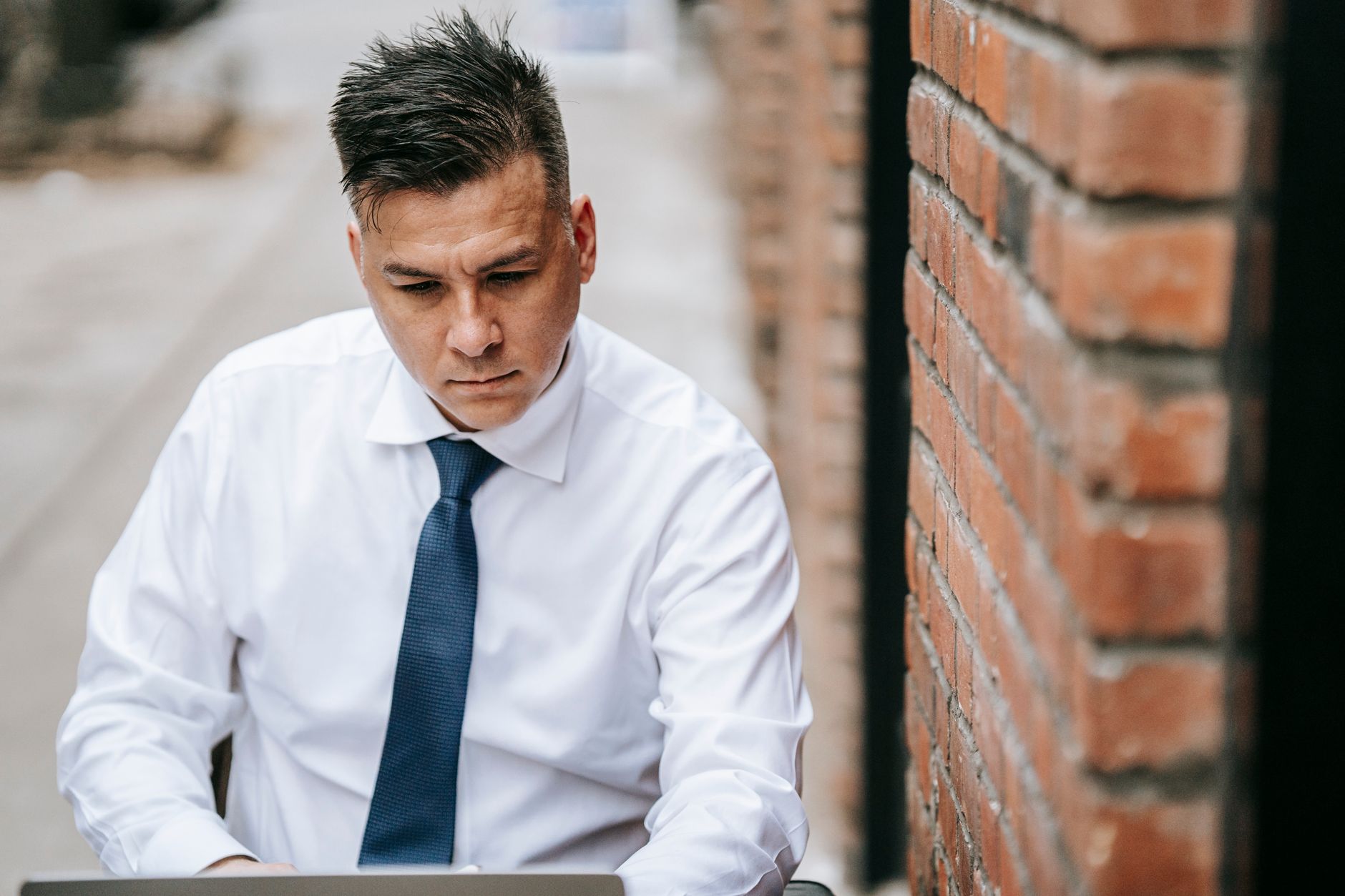 Professional man in shirt and tie working on laptop outdoors, focused and serious.