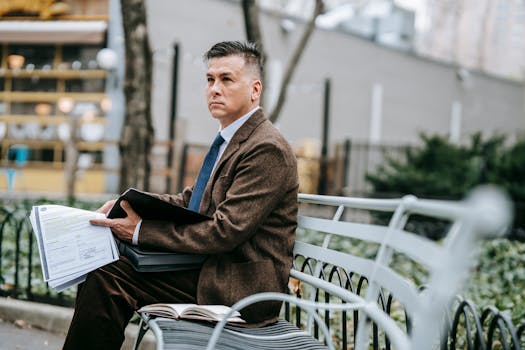 A professional man in formal wear reviewing documents while sitting on a park bench.