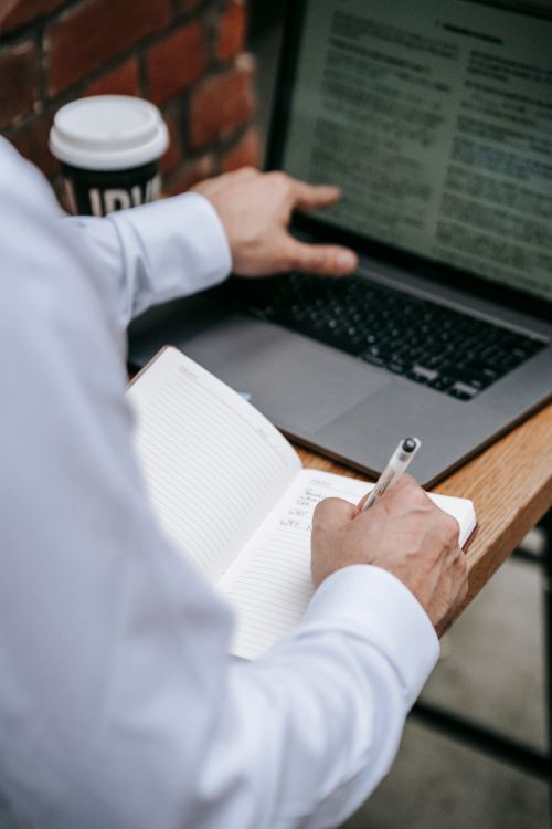 Free Business professional writing notes and working on a laptop at an office desk. Stock Photo