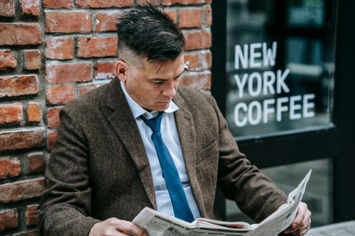 Free Man in formal attire reading a newspaper outside New York coffee shop. Stock Photo