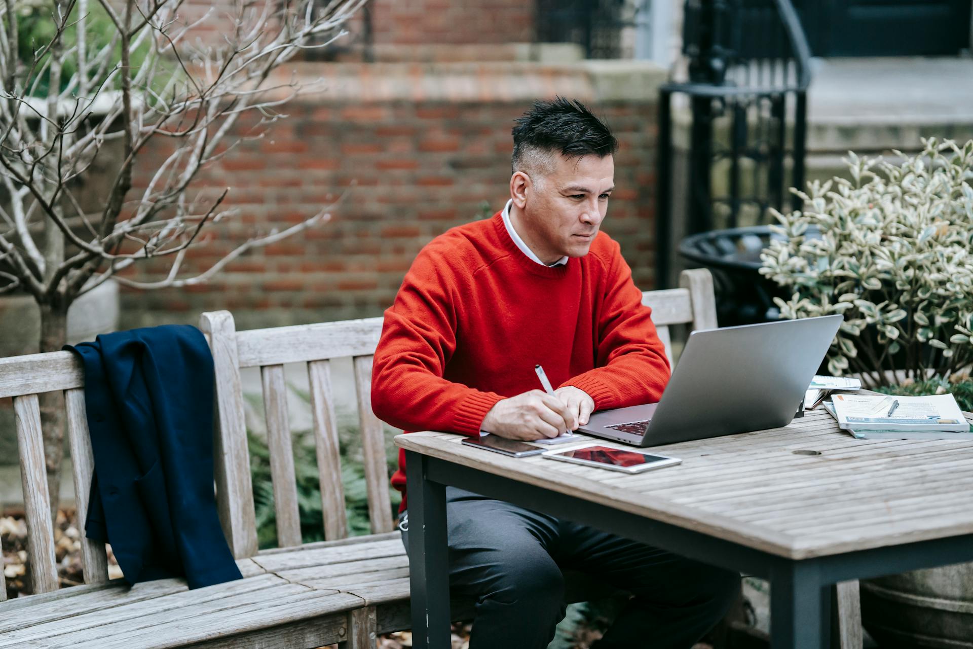 Professional adult working remotely on a laptop outdoors, engaging in digital tasks at a wooden table.