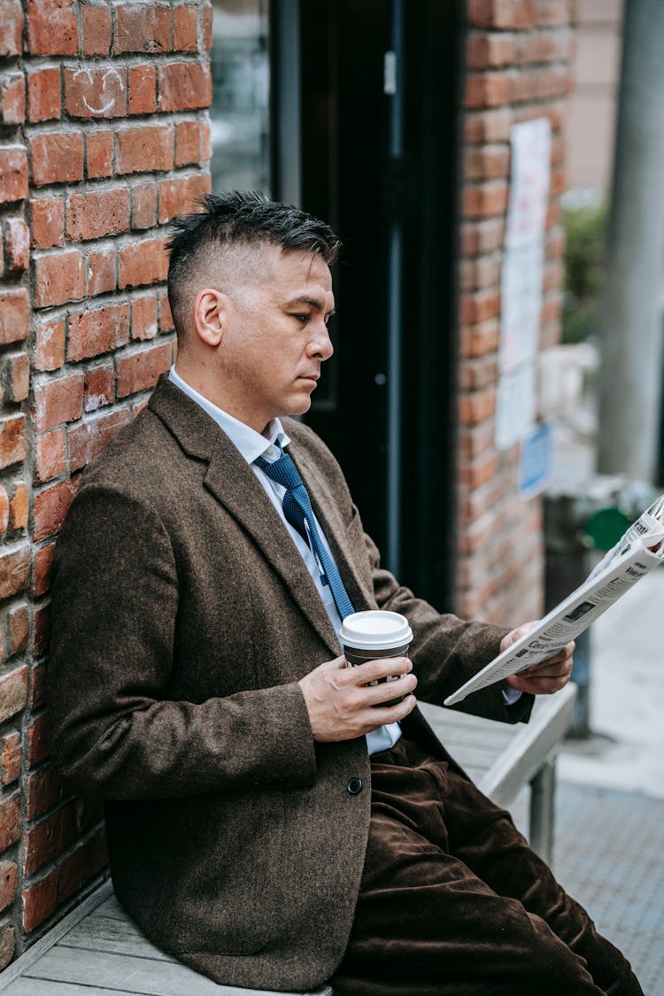 Photo Of Man Reading Newspaper While Holding Drink