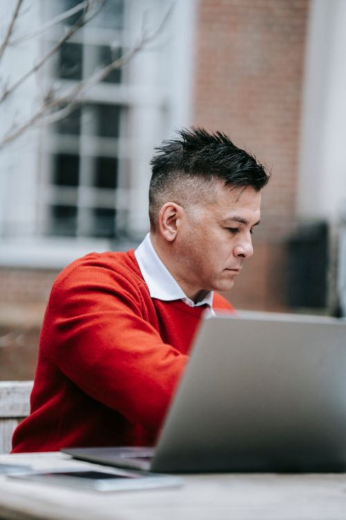 Free A focused professional man working on a laptop outdoors in a casual setting. Stock Photo