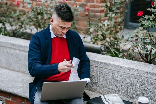 Free Professional man multitasking with laptop and paperwork in an urban outdoor setting. Stock Photo