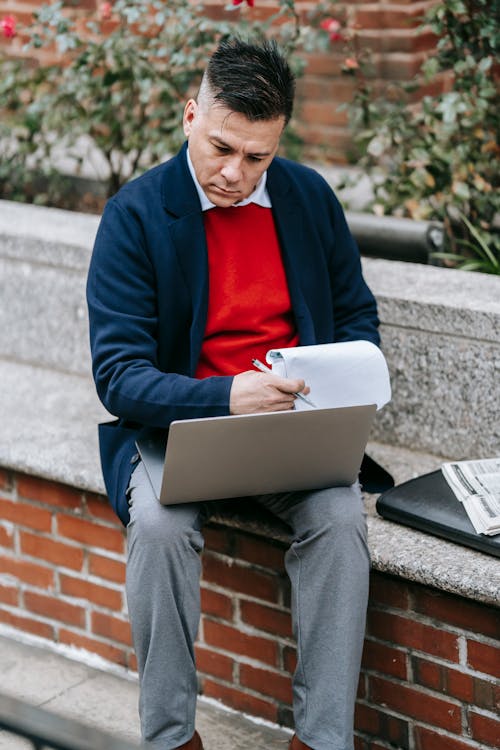 Photo Of Man Looking On Laptop While Holding Papers