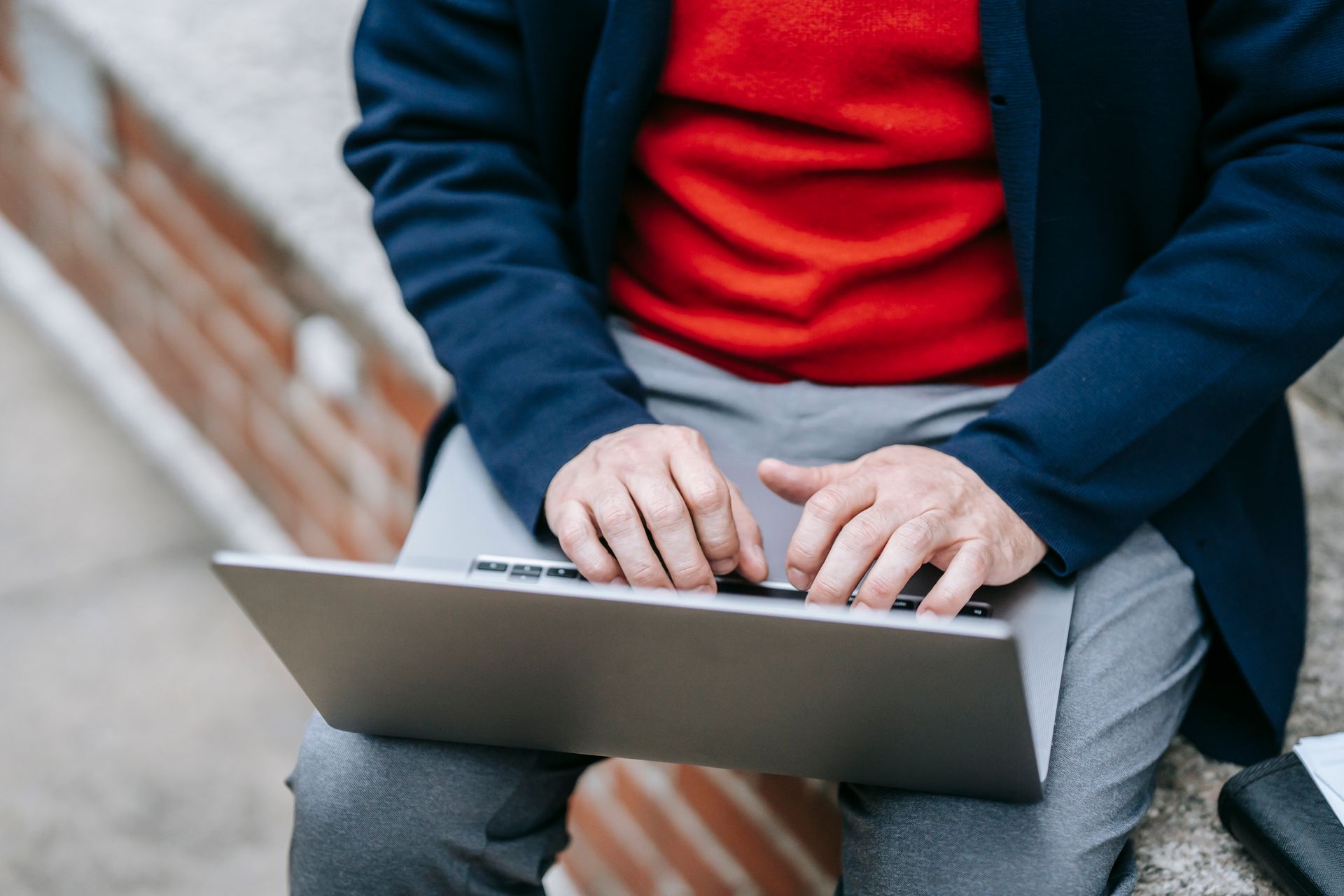 An adult using a laptop outdoors, engaged in remote work on a sunny day.