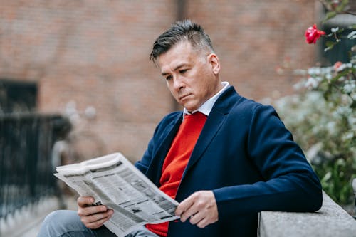 Photo Of Man Reading Newspaper While Leaning On Concrete Surface