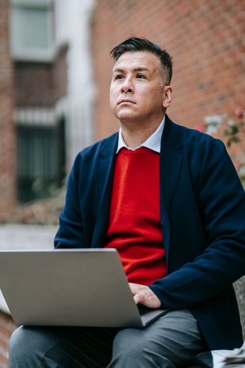 Free A stylish man working outdoors with a laptop, embodying modern remote work culture. Stock Photo