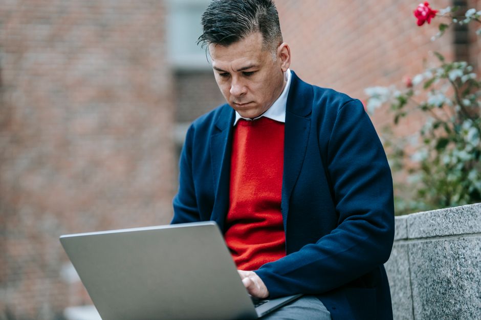 Business professional in red sweater using a laptop outdoors against a brick wall. Business professional in red sweater using a laptop outdoors against a brick wall.