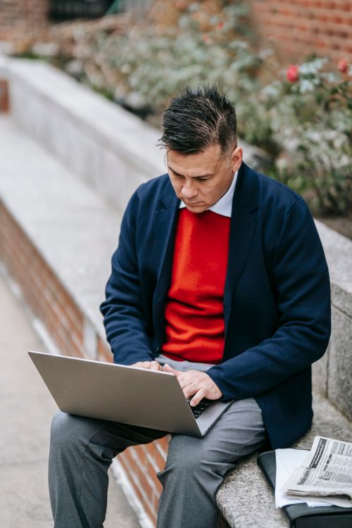 Free Professional man sitting outdoors using a laptop for remote work. Stock Photo