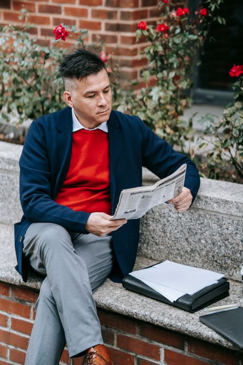Free Professional man in urban setting reading a newspaper on a bench with roses in the background. Stock Photo