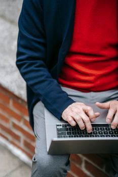 Adult man in red sweater using laptop outside on a bench.