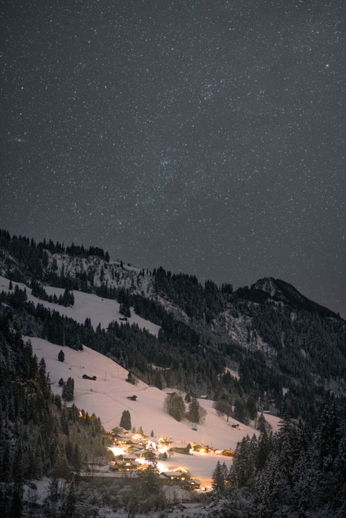 Free A serene mountain village blanketed in snow under a starry night sky, creating a scenic winter landscape. Stock Photo