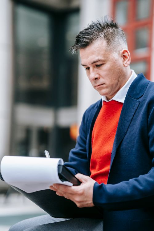 Free Focused male professional writing notes outdoors in a bustling city environment. Stock Photo