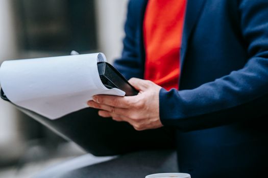 A professional adult outdoors in a suit jacket, focused on reviewing paperwork, highlighting modern business style.
