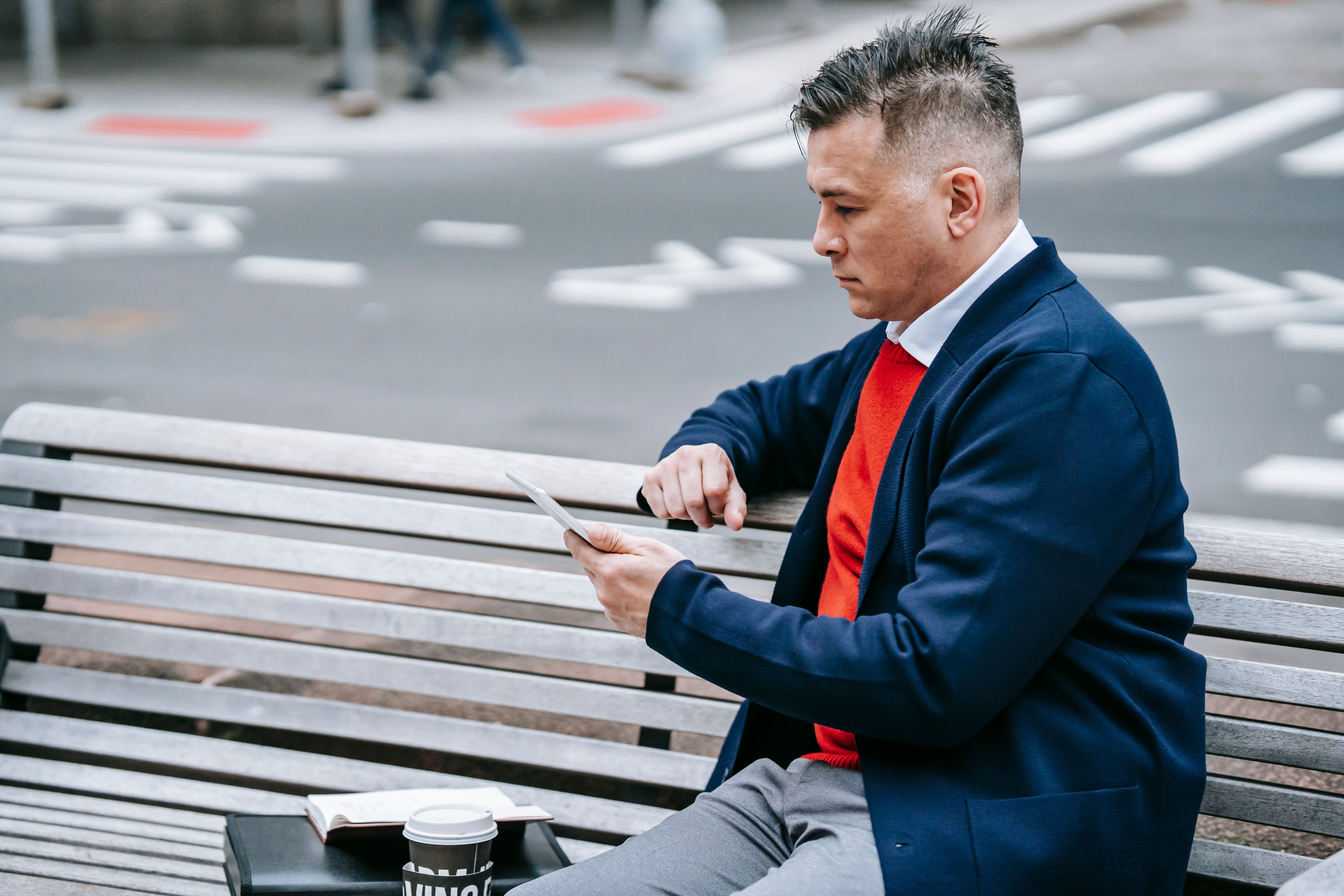 Professional man using tablet on a city bench while enjoying outdoor urban environment.