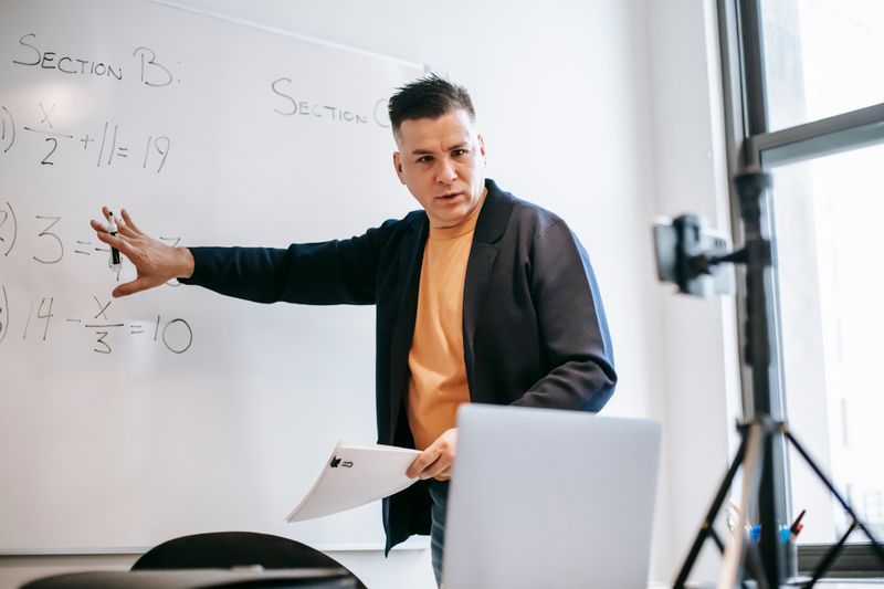 Instructor working through equations at a whiteboard while filming a lesson. Photo by Vanessa Garcia on Pexels