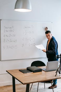 Math instructor teaches equations on a whiteboard using a laptop and tripod setup.