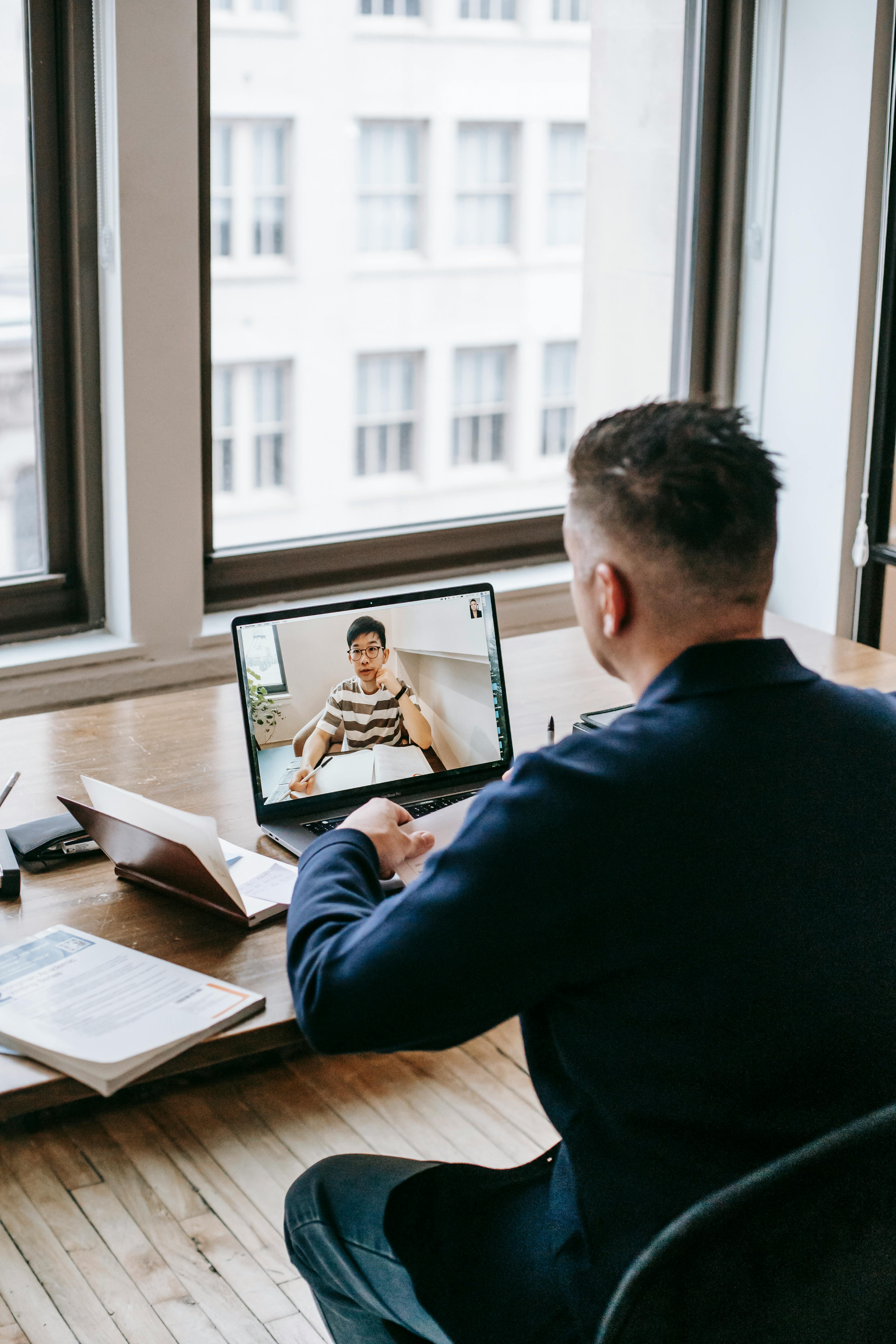 Businessman engaged in a video call at a wooden desk in a bright office.
