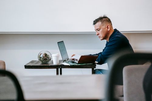 Free A man intently working on a laptop in a modern office setting, showcasing concentration and professionalism. Stock Photo