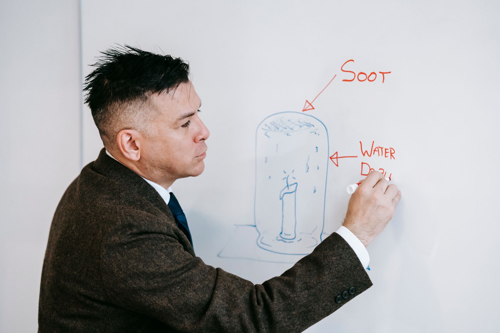 Educator illustrating scientific concepts on whiteboard with marker, explaining soot and water displacement.
