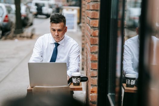 Businessman in formal attire working remotely on his laptop at an outdoor cafe setting.