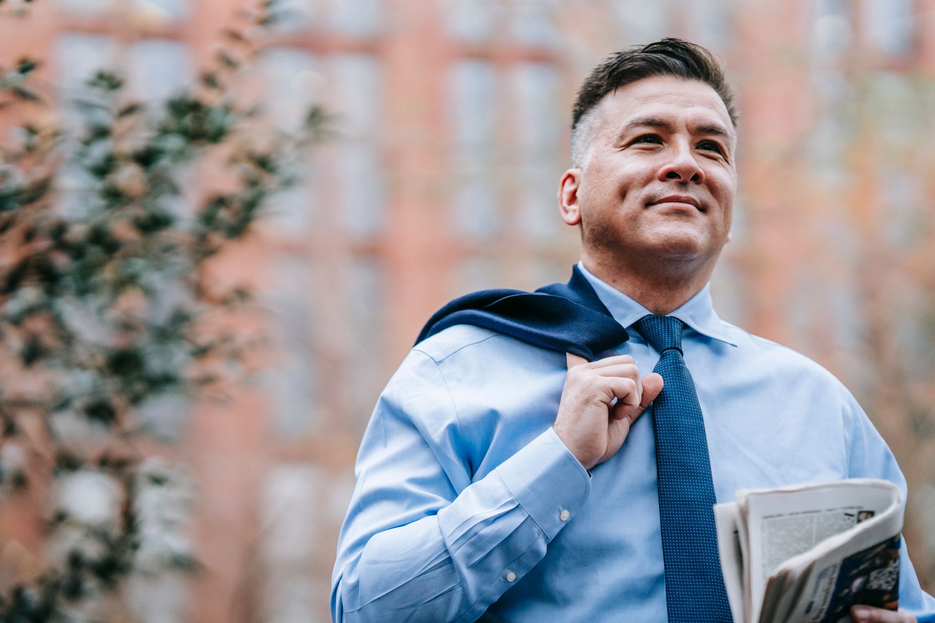 Smiling professional man in formal attire with newspaper, exuding confidence outdoors.