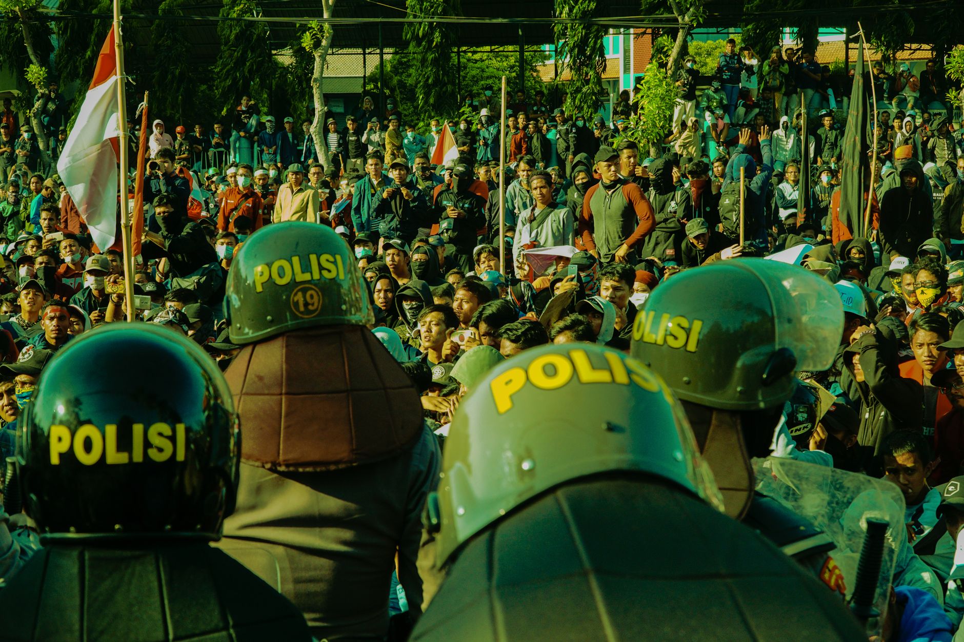 A dynamic scene of a large crowd protesting with police presence wearing helmets marked 'Polisi'.