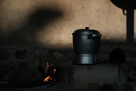 A traditional cooking pot sits on an open fire against a rustic wall.