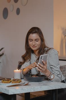 A woman dining and using a smartphone by candlelight, creating a cozy ambiance.