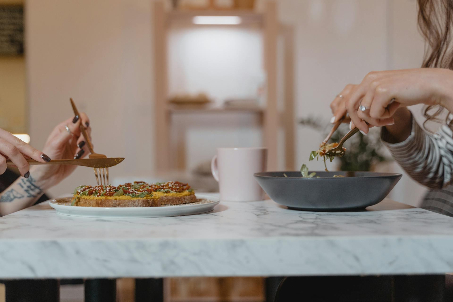 Person Holding Fork and Knife Slicing Food on White Ceramic Plate