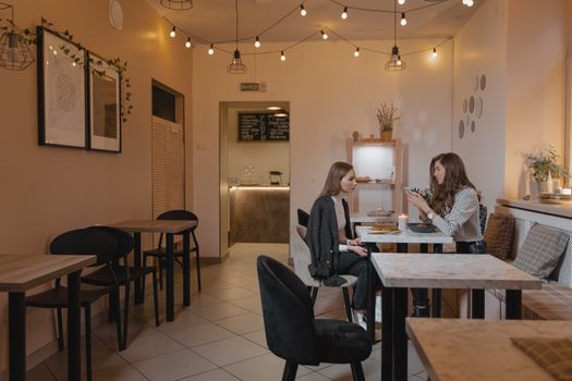 Two women enjoying a meal in a cozy, string-lit cafe setting.