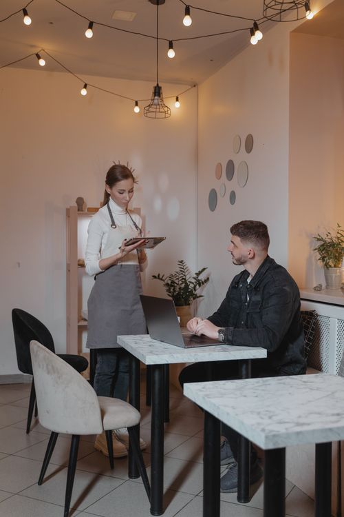 Free A waitress and customer engage in a modern café, highlighting hospitality and technology. Stock Photo