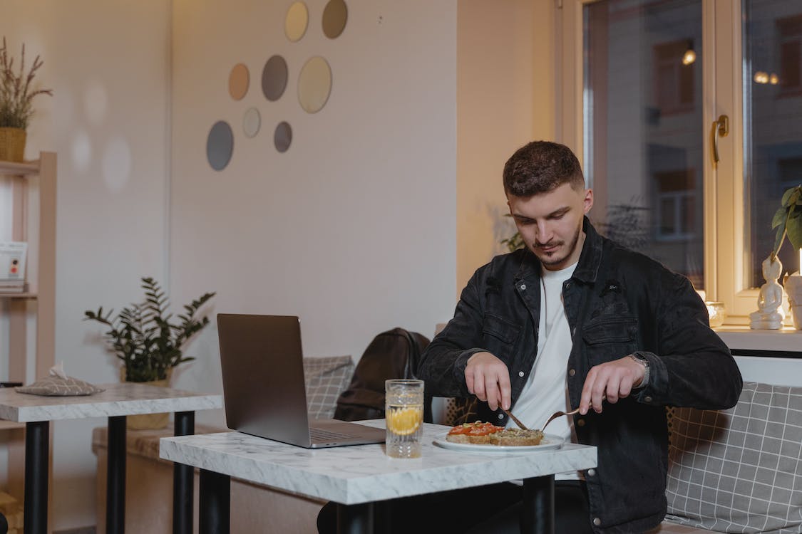 Free A Man in Black Jacket Slicing His Food while Sitting on the Table Stock Photo
