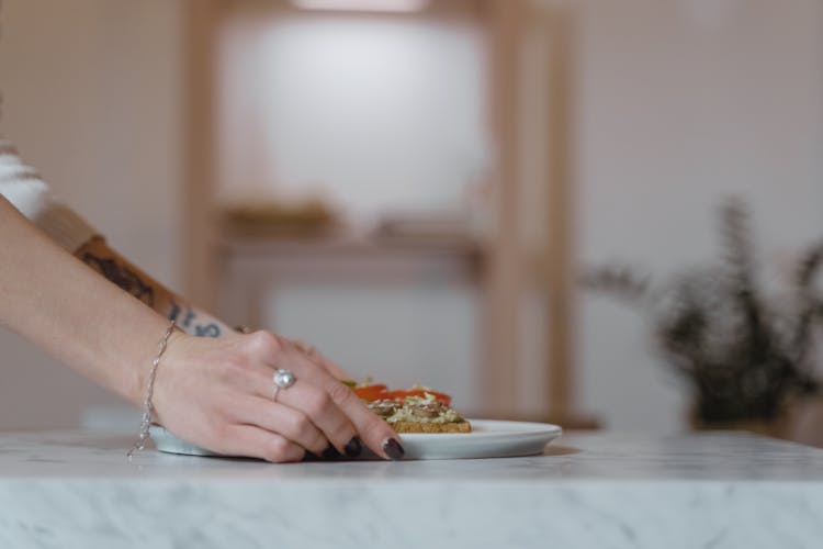 A Person Wearing A Silver Ring And Bracelet Holding A Plate With Food On The Table