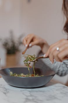 Close-up of a vegetarian salad being served in a dark bowl on a marble table.