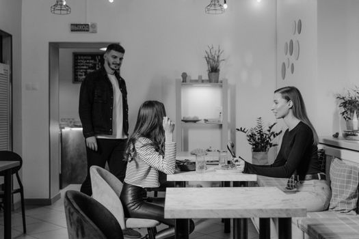 A black and white scene of three adults socializing in a stylish cafeteria setting.