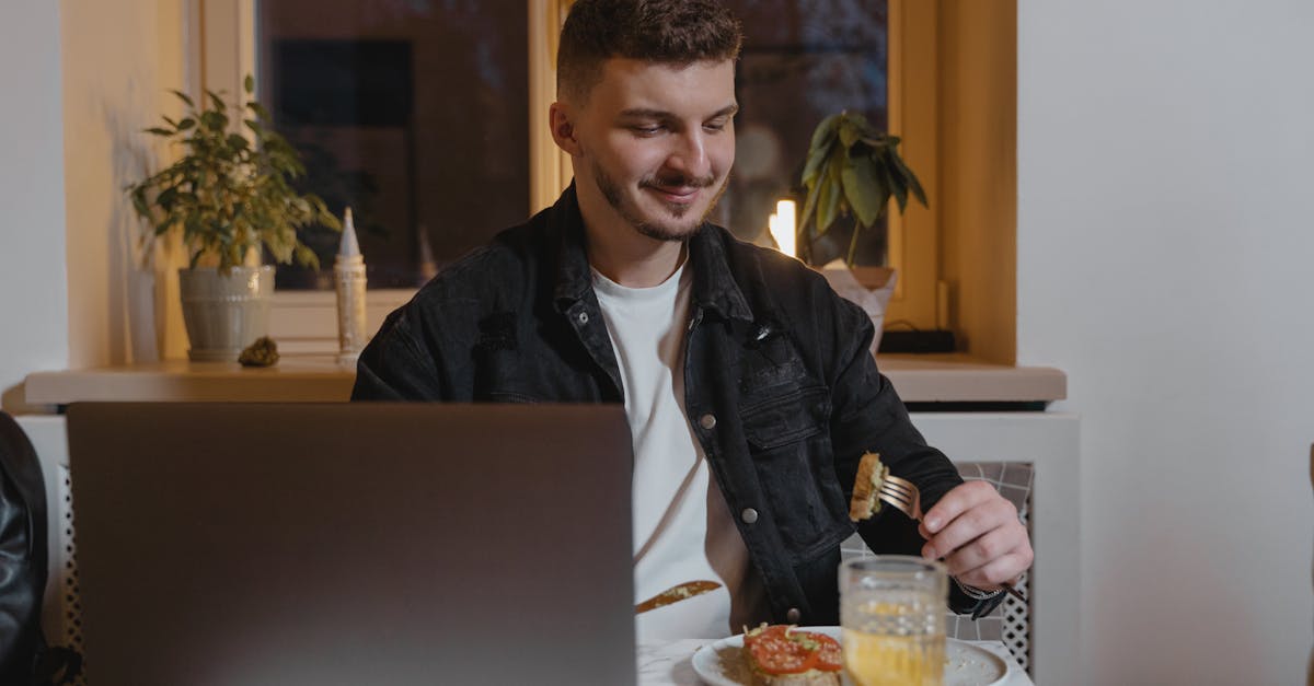 Adult enjoying a snack while working on a laptop at home.