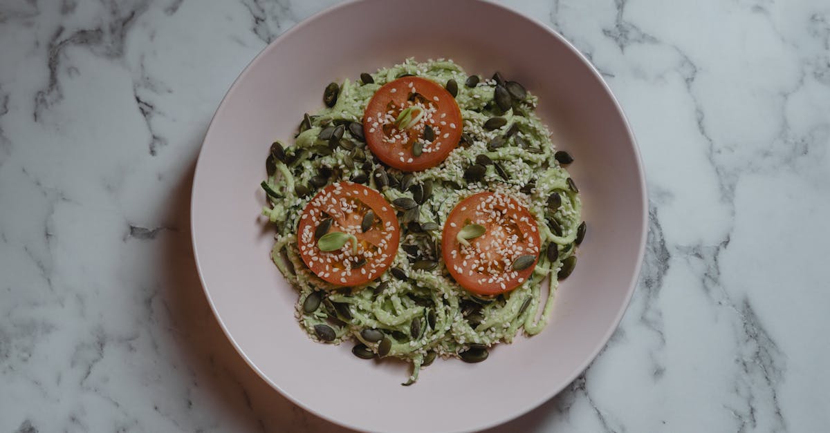 Colorful vegan meal featuring zucchini noodles, tomato slices, and seeds on a marble top.
