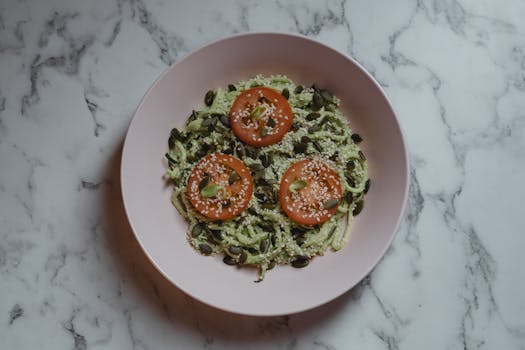 Colorful vegan meal featuring zucchini noodles, tomato slices, and seeds on a marble top.