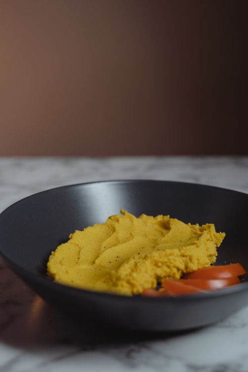 Free Smooth and creamy homemade hummus served in a black bowl with sliced tomatoes, perfect for a healthy snack. Stock Photo