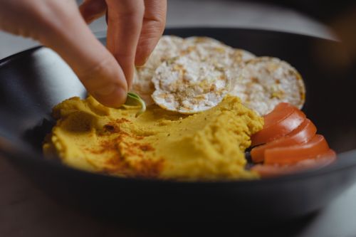 Free A delightful vegan snack featuring creamy hummus, rice cakes, and fresh tomato slices served in a stylish black bowl. Stock Photo