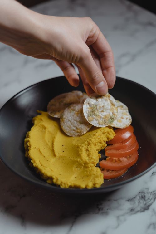 Free Hand serving crackers with hummus and tomatoes on a marble surface. Stock Photo