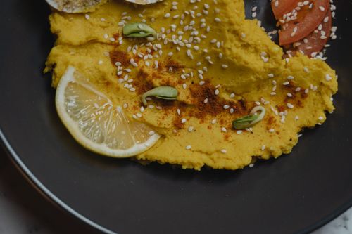 Free Close-up of creamy hummus with lemon slices and sesame seeds on a black plate. Stock Photo