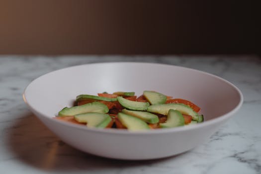 A delicious vegan salad featuring sliced avocado and tomatoes on a marble table.