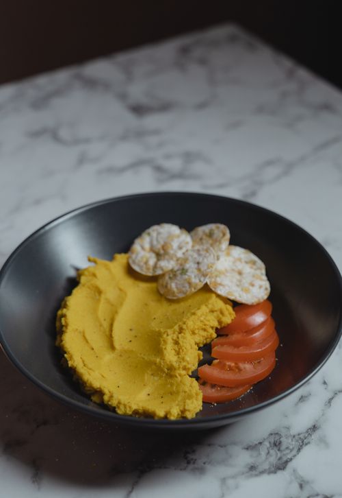 Free Delicious vegan hummus served with crispy crackers and fresh sliced tomatoes on a marble surface. Stock Photo